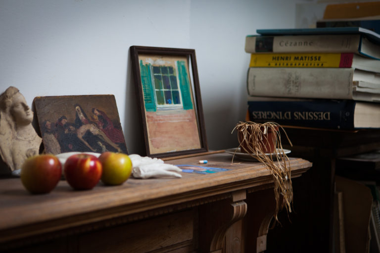 Lennart Anderson studio interior mantle with painting, apples, dry plant, and stacked books