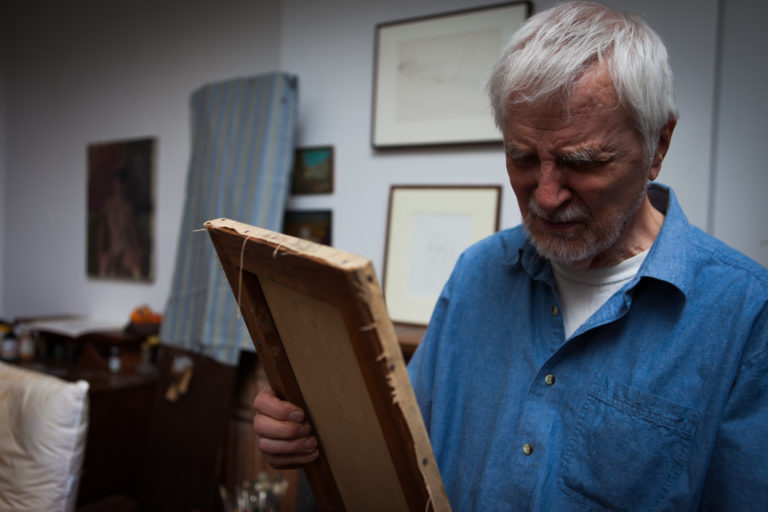 Lennart Anderson in his studio looking at a painting that he is holding in his hands