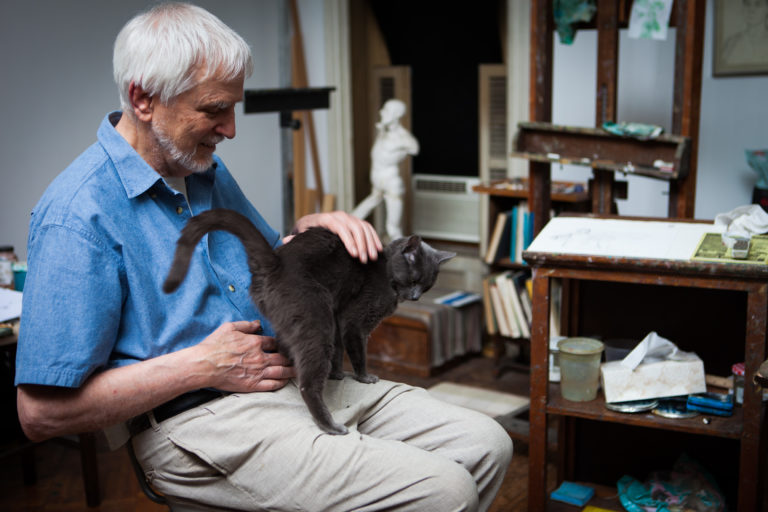 Lennart Anderson sitting in his studio with gray cat on his lap