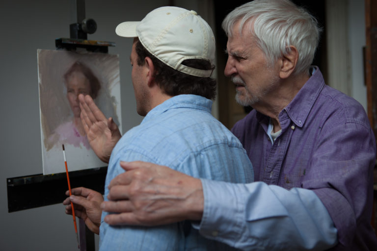 Lennart Anderson in his studio with arm around artist Brian Schumacher critiquing a painting.