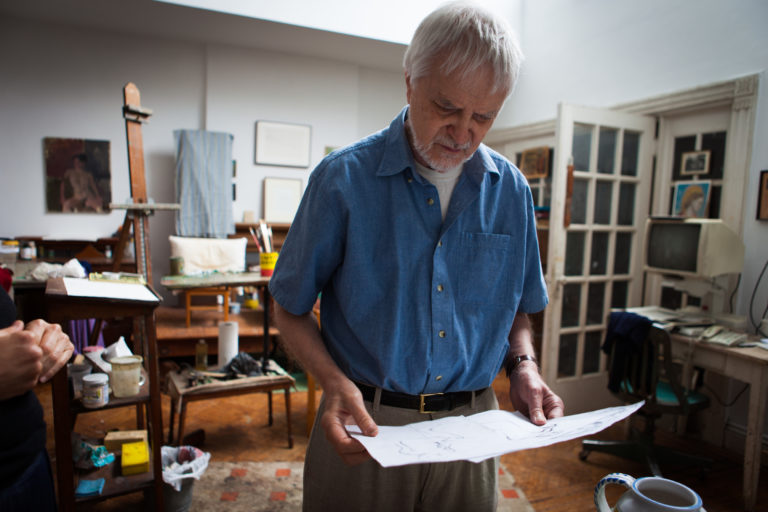 Lennart Anderson in his studio, standing, looking down at several drawings that he is holding in his hands