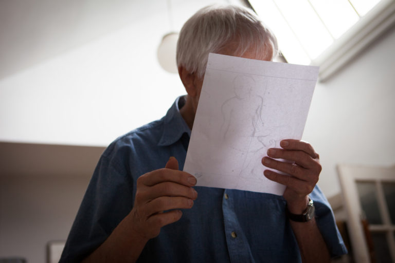 Lennart Anderson in his studio taken from below, with Lennart looking closely at a drawing that he is holding in his hands