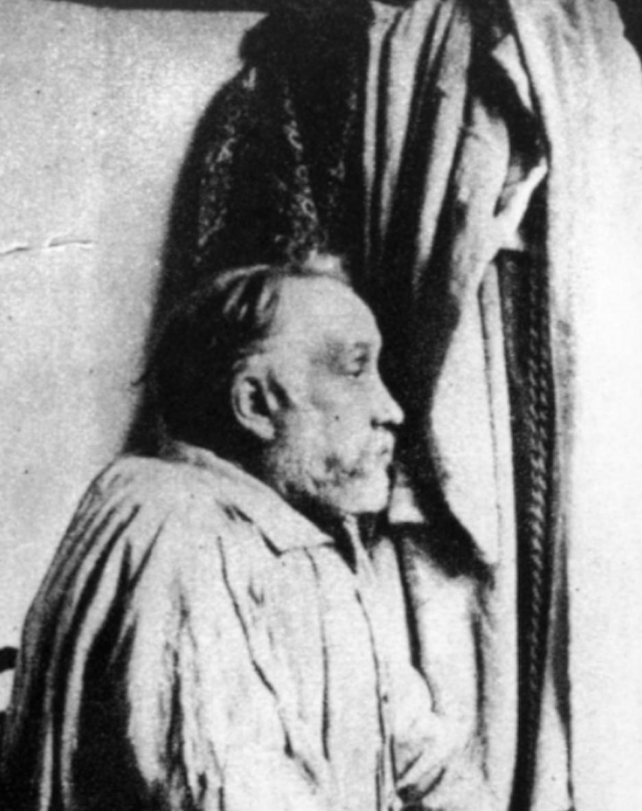 Black and white photograph of Edgar Degas in profile view in his studio, looking right, in a loose fitting smock