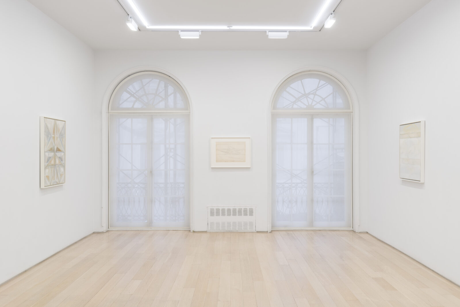 A luminous room with two floor to ceiling windows at the far end and three three abstract paintings on three different walls.